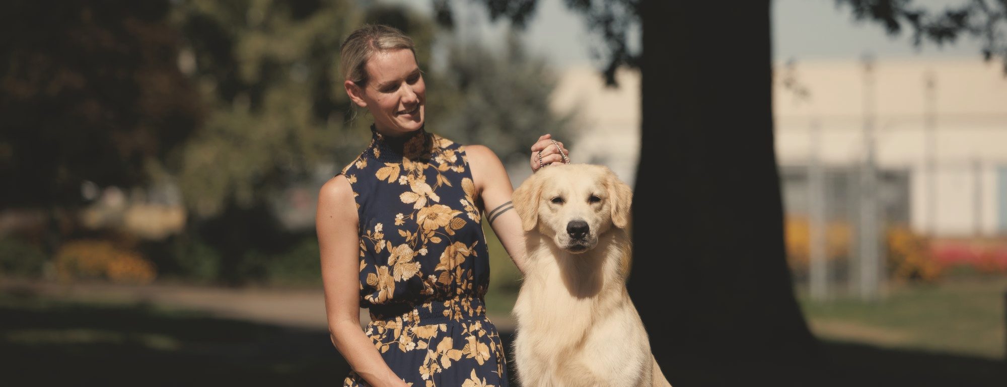 A woman kneeling beside her golden retriever in autumn light