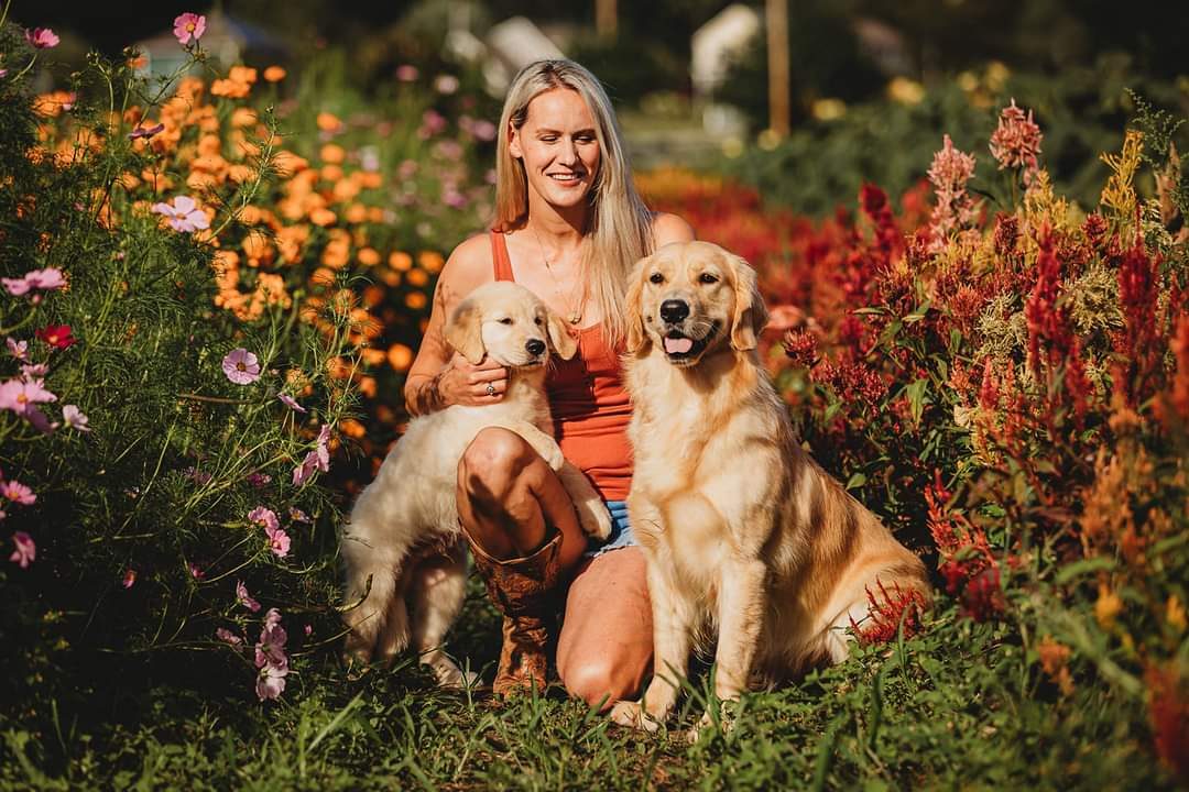 The founder in a flower field with two golden retrievers