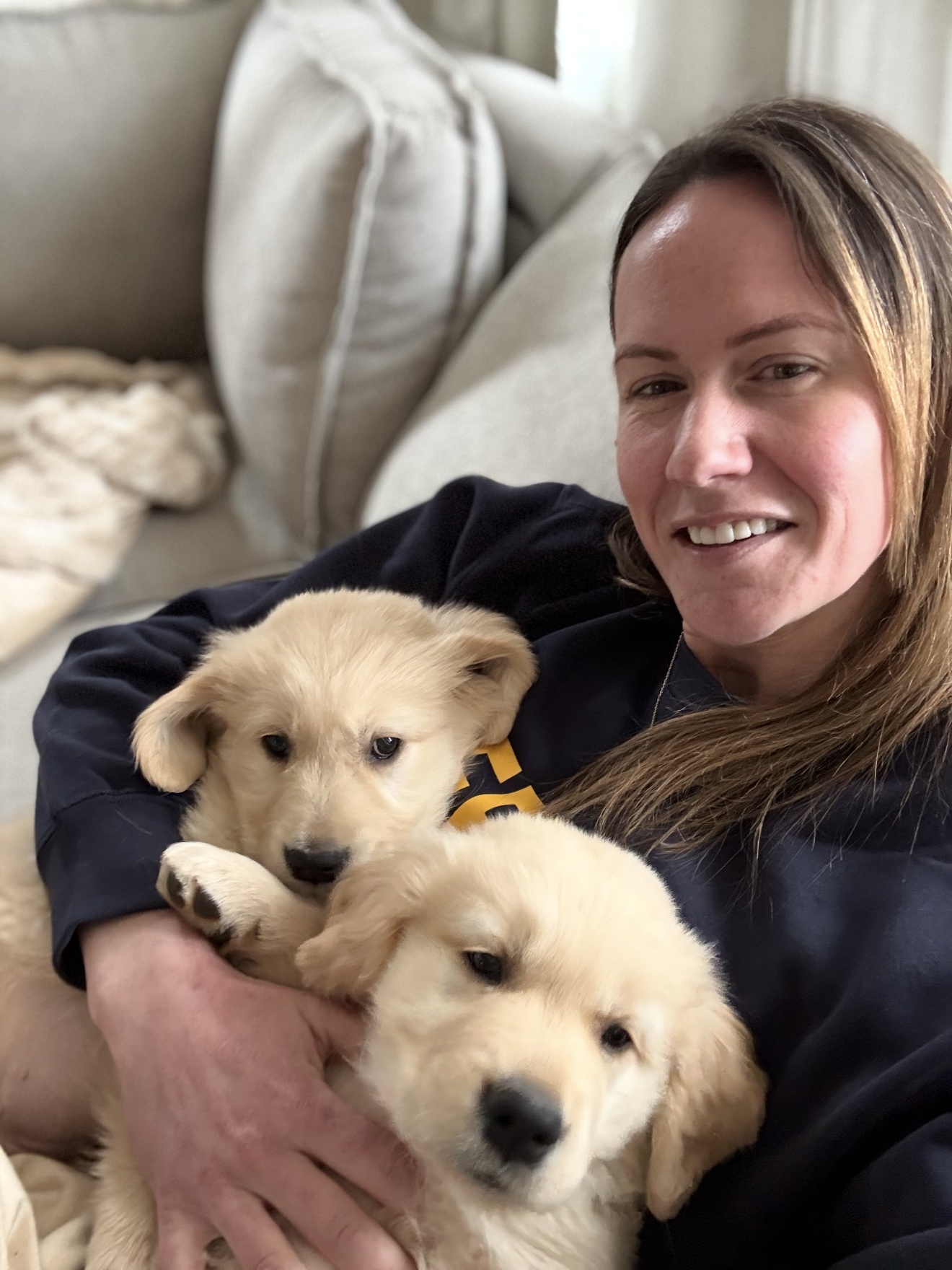 Amanda on a sofa at home with two Golden Retriever puppies in her arms